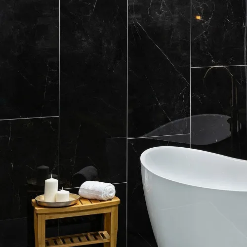 Modern bathroom with white freestanding tub, rolled towel, candles on wooden stool, and black marble walls.
