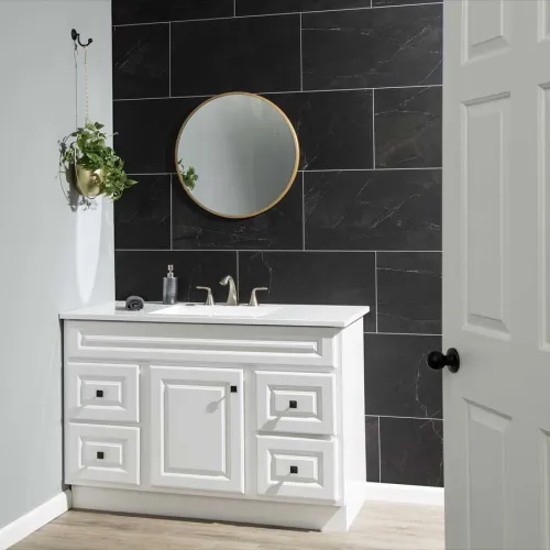 Modern bathroom vanity with white cabinet, round mirror, black tile wall, and hanging plant on side wall.