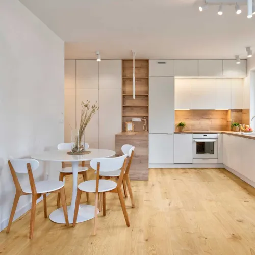 Bright modern kitchen with white cabinets, wooden accents, round dining table, and light wood flooring.
