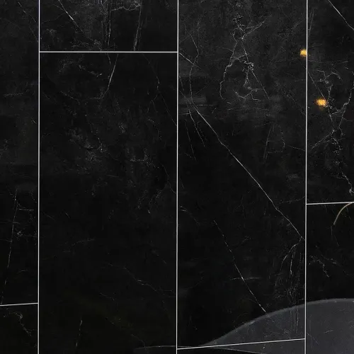 Glossy black marble wall with white veining and tile grout lines, reflecting subtle light spots.