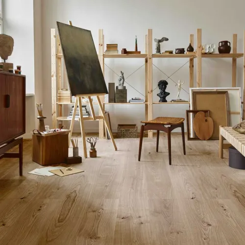 Art studio with wooden flooring, easel, sculptures, bookshelves, and minimalist decor in natural light.
