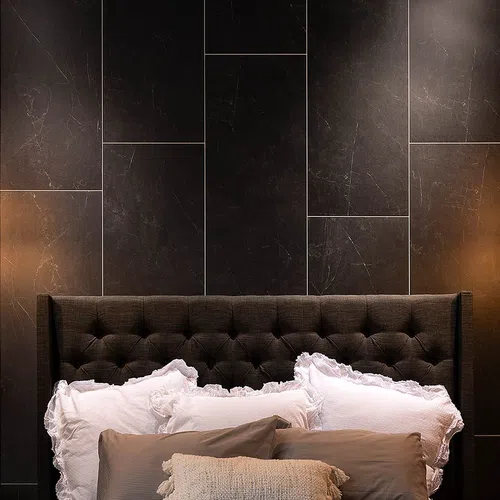 Dark tufted headboard with white ruffled pillows and textured beige throw pillow against black marble wall.