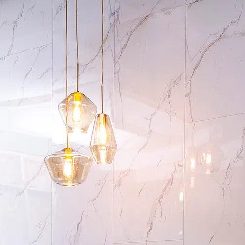Three modern glass pendant lights glowing against white marble wall with grey veins in minimalist interior.