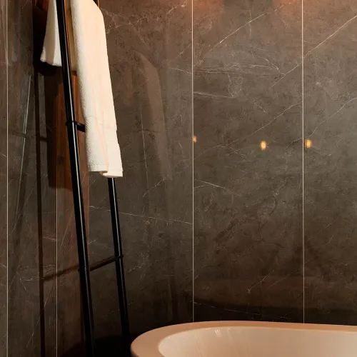 Modern bathroom with dark marble walls, white freestanding tub, and a black metal towel ladder holding a white towel