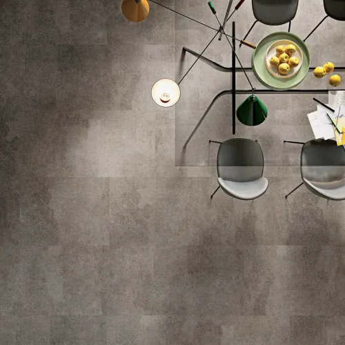 Top view of a modern dining table with black chairs, a green lamp, and a bowl of yellow lemons on a gray floor.