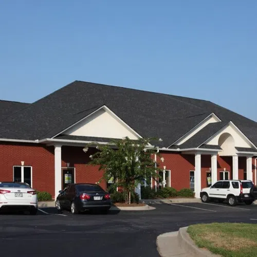 Single-story red brick commercial building with pitched roof, parking lot, and four parked vehicles on a sunny day