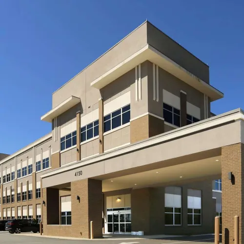Modern three-story office building with large windows, brick accents, and covered entrance on a clear sunny day.