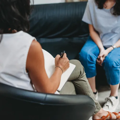 Therapist taking notes during a counseling session with a woman sitting on a sofa in a modern office.