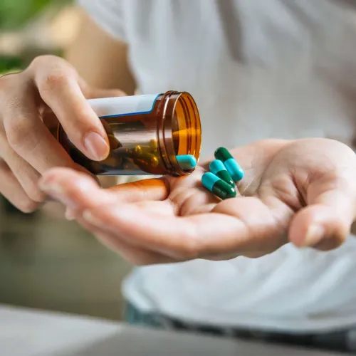 Person pouring green and blue capsules from a brown medicine bottle into an open hand.