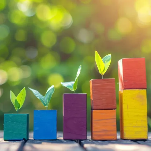 Colorful wooden blocks stacked with green plant sprouts symbolizing growth and progress on a wooden surface.