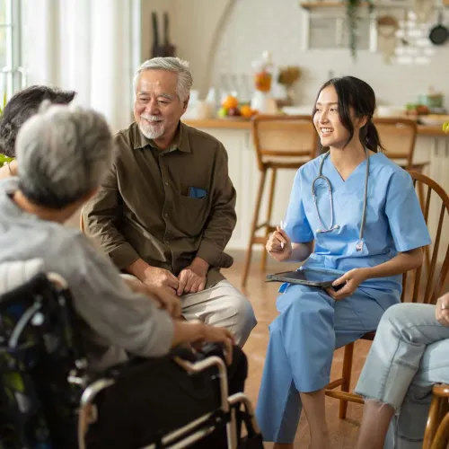 Nurse in blue scrubs engaging warmly with elderly patients in a cozy, home-like setting during group care.