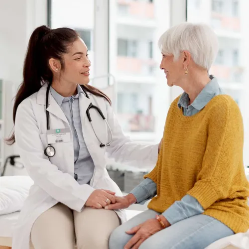 Doctor in white coat comforting senior woman patient during consultation in bright medical office.