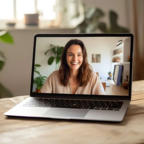 Smiling woman in striped shirt on laptop screen during video call in a cozy home office setting.