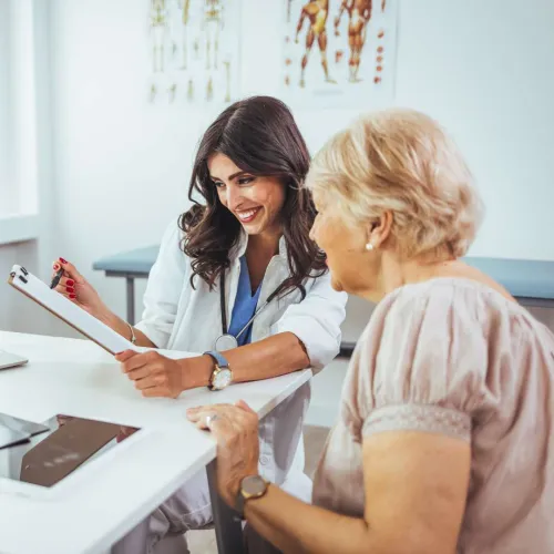Female doctor smiling and explaining medical information to an elderly woman in a clinic setting.