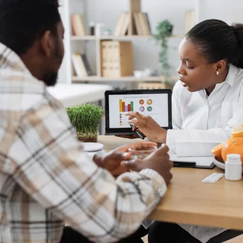 Nutritionist explaining a healthy balanced diet with colorful charts on a tablet to a man in a consultation.