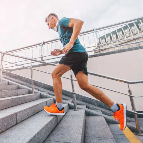 Man in orange running shoes climbing outdoor stairs during daytime workout in urban environment.