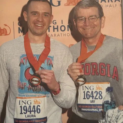 Two marathon finishers wearing medals and race bibs smiling in front of a marathon backdrop at the ING Georgia Marathon.