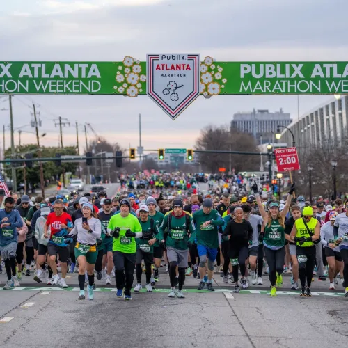 Runners start the Publix Atlanta Marathon weekend race under green banner on city street at dawn.