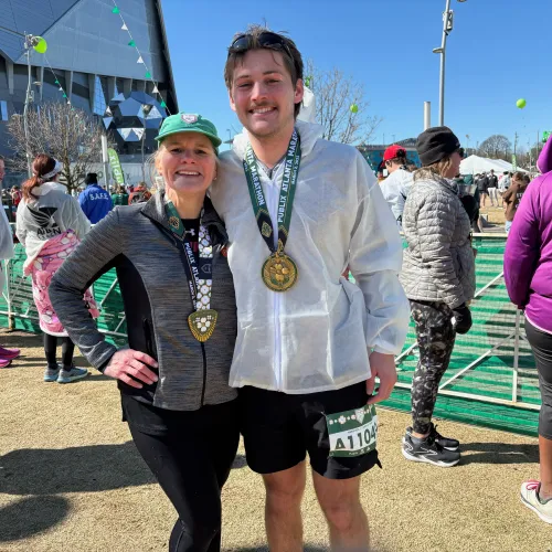 Two marathon runners smiling with medals at race finish line in sunny outdoor event