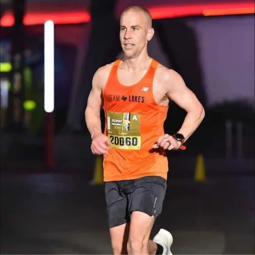 Runner in orange Team Luke's tank top and black shorts racing at night wearing bib number 20060.