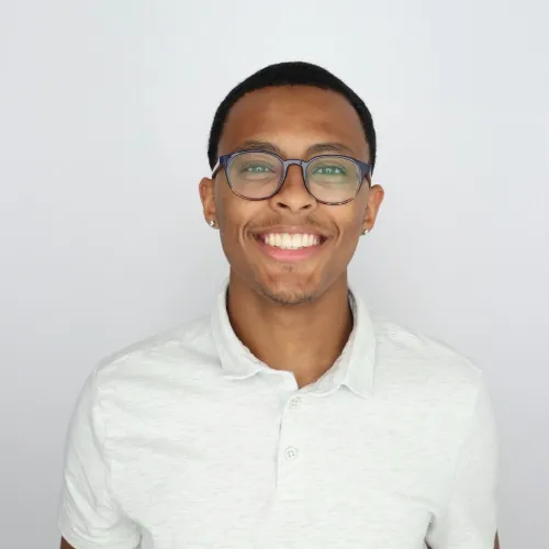 Smiling young man wearing glasses and a white polo shirt against a plain light gray background