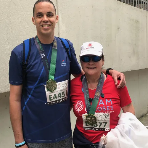 Two marathon finishers wearing medals and race bibs pose smiling against a concrete wall after the race.