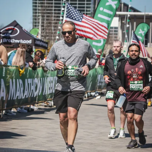 Runners crossing the finish line at a marathon event with spectators and American flags in the background