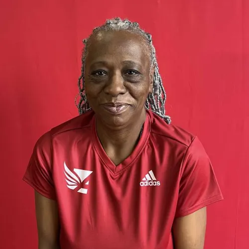 Smiling woman with gray braided hair wearing red Adidas shirt against a red background