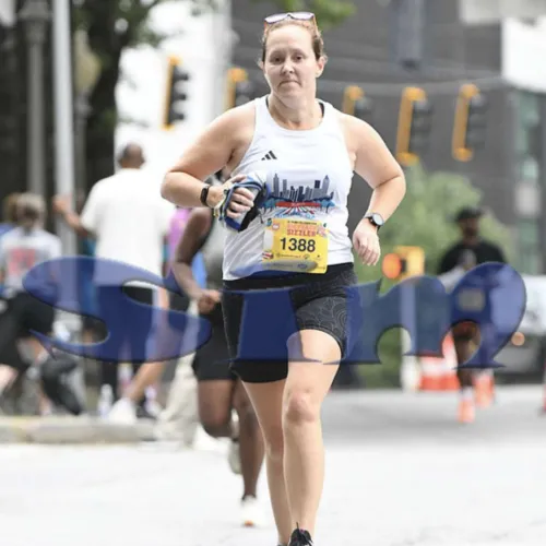 Female runner wearing bib 1388 participating in a city road race on an urban street.
