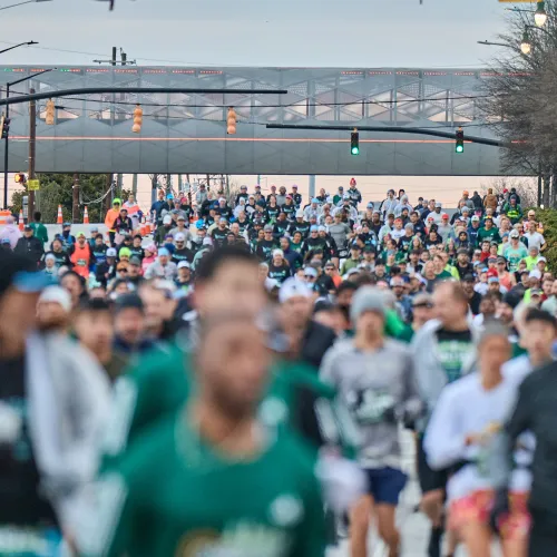 Large crowd of runners participating in a road race event on a city street under traffic lights.