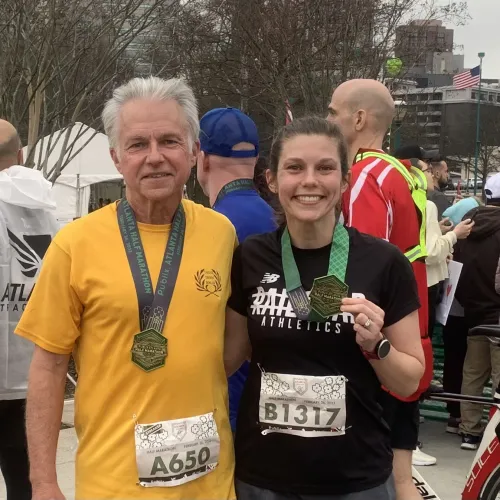Two runners proudly display medals and race bibs after finishing a marathon, smiling at the camera.