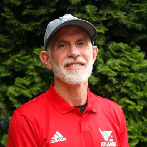 Smiling elderly man wearing a red Adidas Atlanta Track Club shirt and gray cap standing outdoors