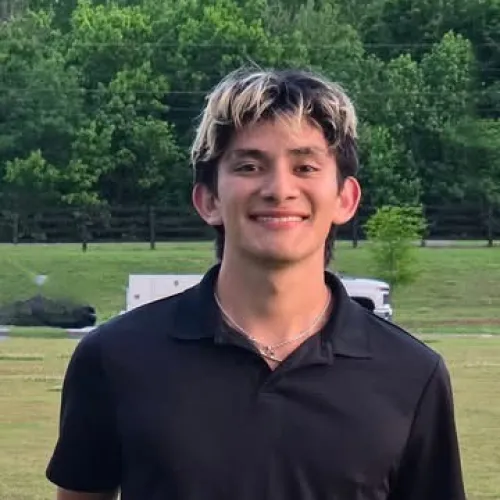 Young man standing on grass holding a Coaches Award plaque with trees in the background on a sunny day