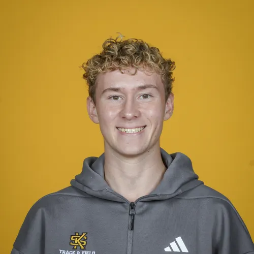 Young man with curly hair wearing a gray zip-up hoodie with Track & Field logo on yellow background