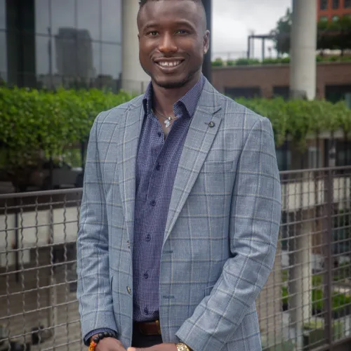 Runner wearing bright green shoes and sunglasses holds a race trophy at a finish line with people and trees in background