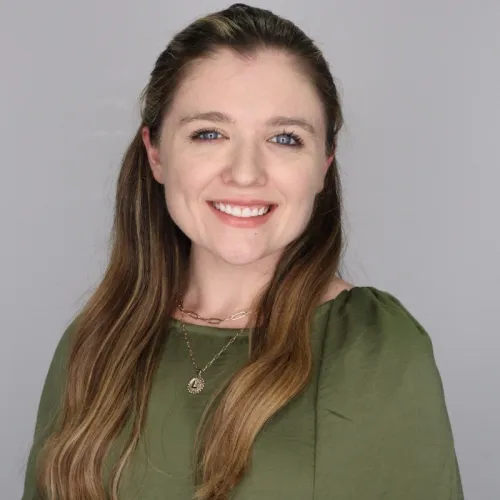 Runner wearing bright green shoes and sunglasses holds a race trophy at a finish line with people and trees in background