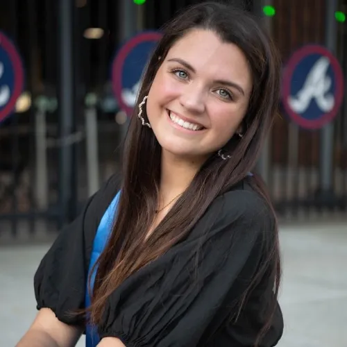 Runner wearing bright green shoes and sunglasses holds a race trophy at a finish line with people and trees in background