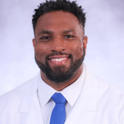 Smiling male doctor with curly hair wearing a white coat and blue tie on a light background