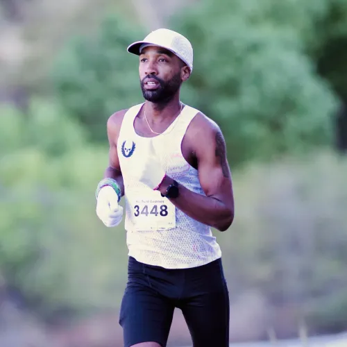 Male runner wearing white cap, tank top, black shorts, and neon green shoes running on a road race with bib 3448.