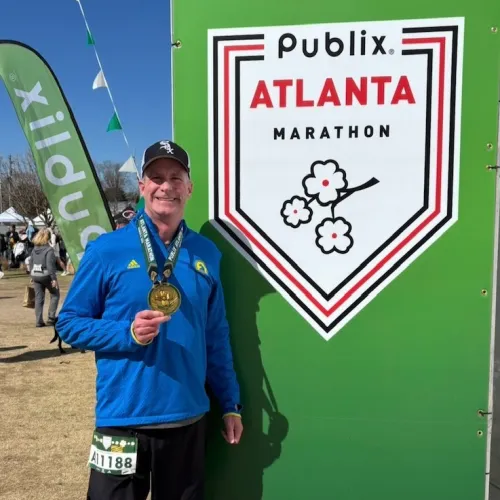 Runner with medal posing in front of Publix Atlanta Marathon sign during event outdoors.