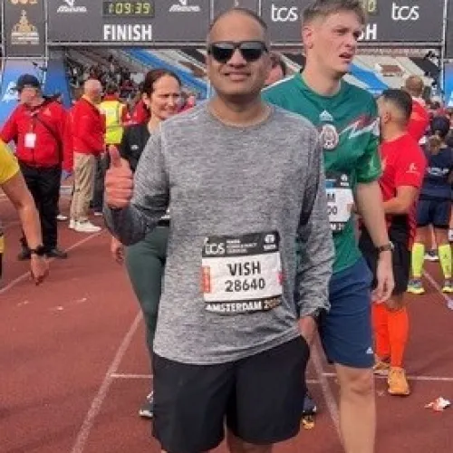 Marathon runners gather at finish line on track with bibs and race gear on a cloudy day.