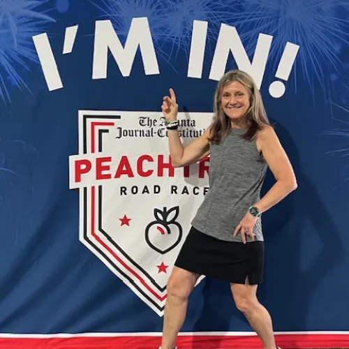 Woman in athletic wear posing and pointing at Peachtree Road Race banner with I'm In text.