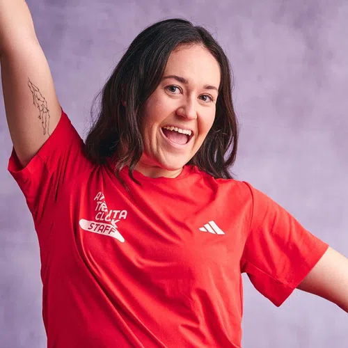 Smiling woman in a red staff t-shirt with her arm raised against a purple background