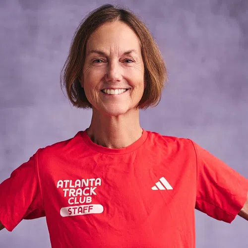 Smiling woman wearing a red Atlanta Track Club staff shirt against a purple background.