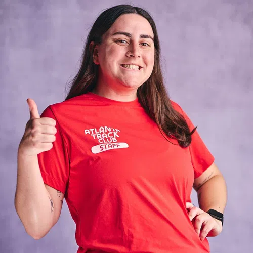 Smiling woman in red Atlanta Track Club staff shirt giving thumbs up against purple background