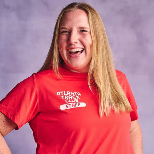 Smiling woman wearing a red Atlanta Track Club staff t-shirt against a soft purple background