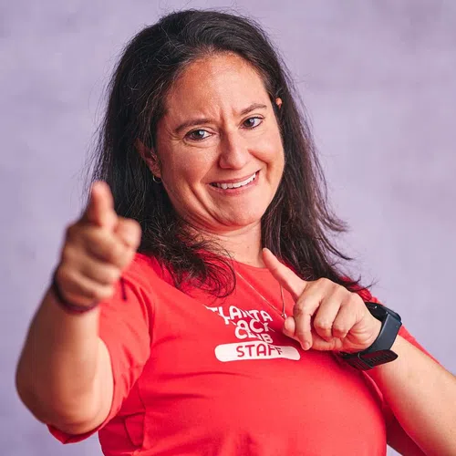 Smiling woman wearing red staff T-shirt pointing playfully at the camera with blurred purple background