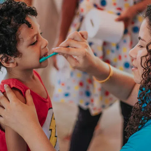 Woman helping young boy brush his teeth during a dental care activity indoors.