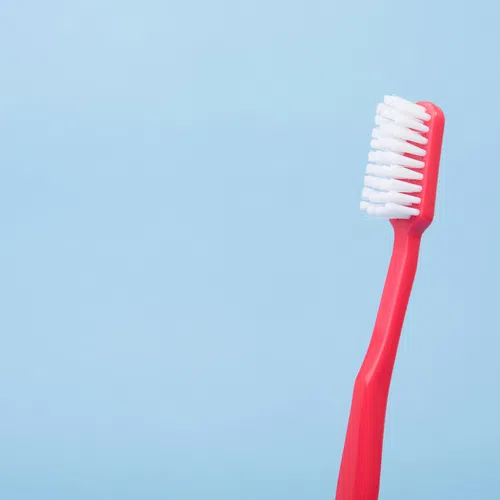 Red toothbrush with white bristles on a light blue background for dental hygiene.