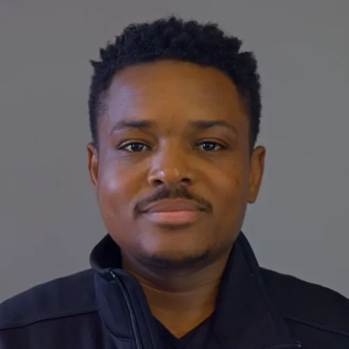 Smiling doctor wearing a white coat and tie, against a gray background.